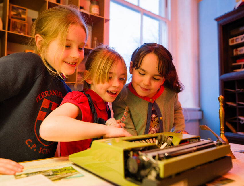 three children smiling crowded around a typewriter