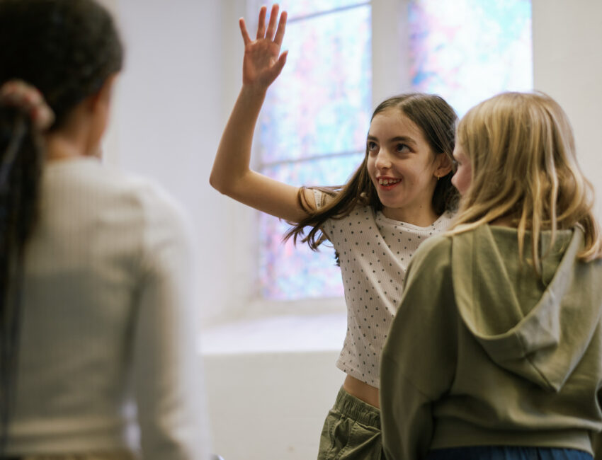 Three children doing drama games. One child has their hand in the air.