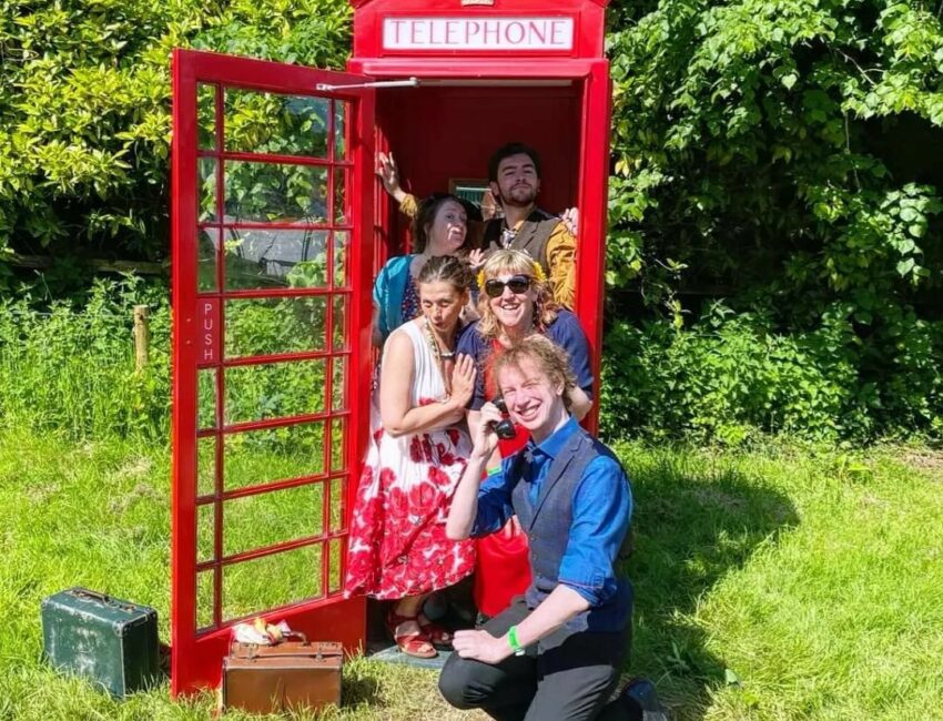 Five performers posing in a red telephone box at Great Estate Festival.