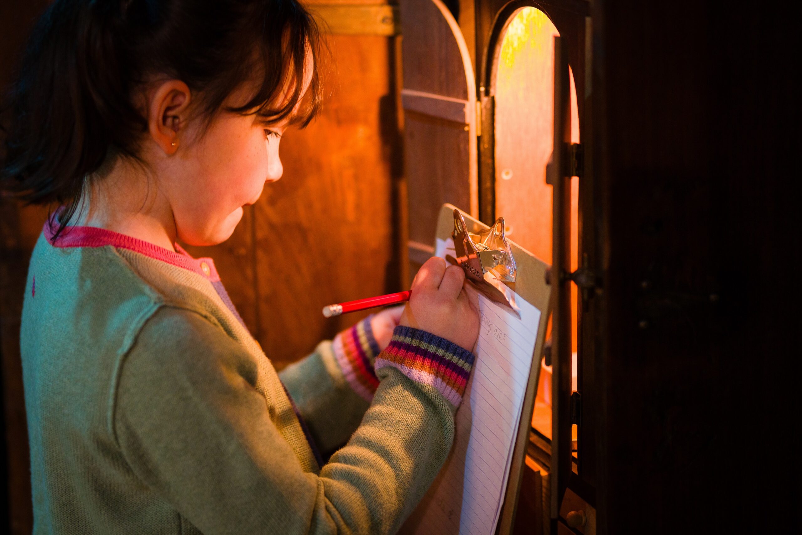 Girl writing on clipboard looking into lit cupboard. Inage by Steve Tanner